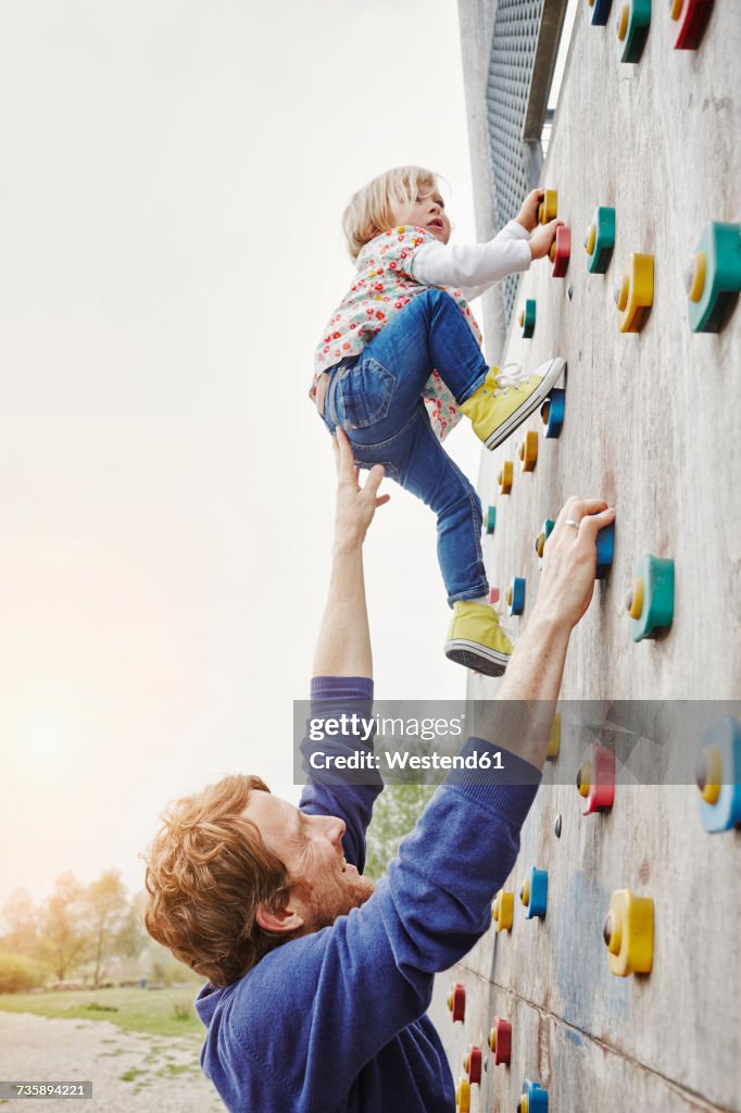 Girl climbing on a wall supported by father