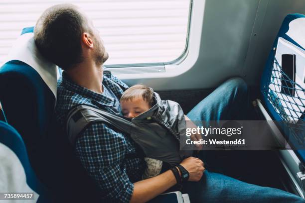 Father on the train holding his sleeping baby in a baby carrier