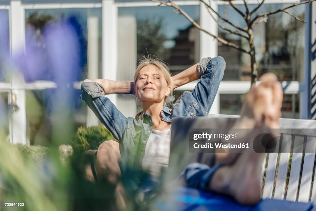 Smiling woman with laptop relaxing on garden bench