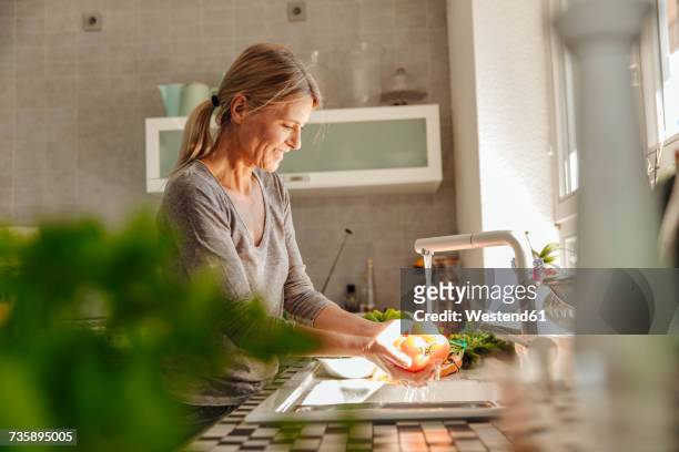 woman in kitchen washing tomatoes - mujer 50 años fotografías e imágenes de stock