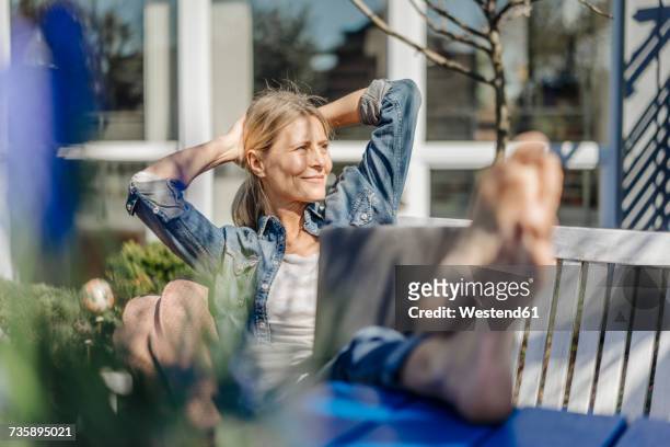 smiling woman with laptop relaxing on garden bench - positive healthy middle age woman stock pictures, royalty-free photos & images