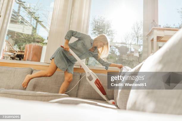 happy woman at home hoovering the couch - vacuum cleaner stock-fotos und bilder