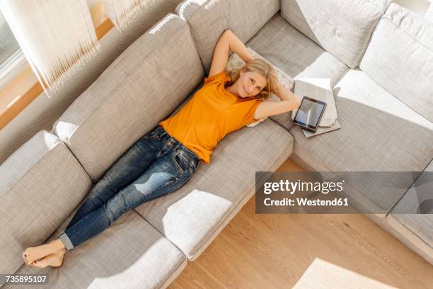 smiling woman at home lying on couch - hands behind head stockfoto's en -beelden