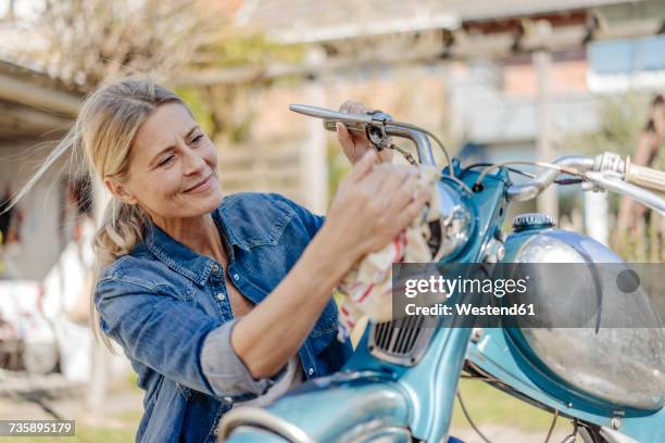 smiling woman cleaning vintage motorcycle - época histórica imagens e fotografias de stock