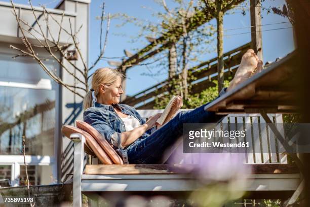 smiling woman reading book on garden bench - garden bench stock pictures, royalty-free photos & images