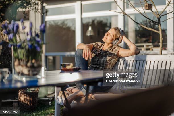 woman wearing headphones relaxing on garden bench - indulgence stockfoto's en -beelden