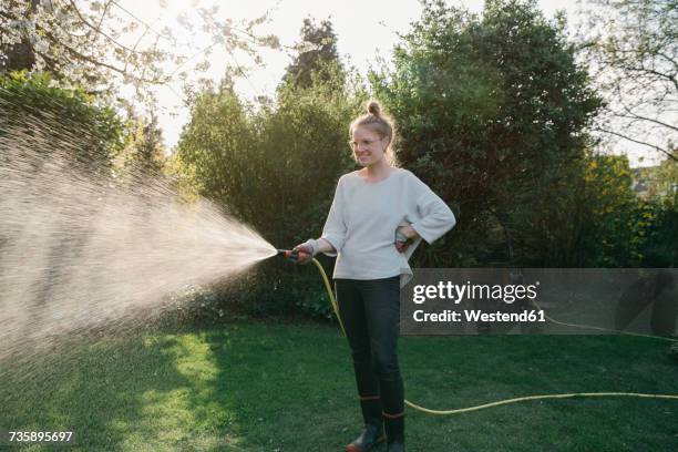 young woman sprinkling lawn in the garden - garden hose foto e immagini stock