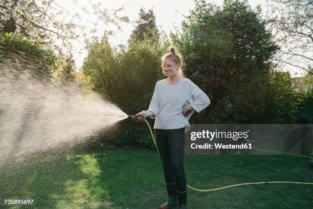 young woman sprinkling lawn in the garden - tuinslang stockfoto's en -beelden