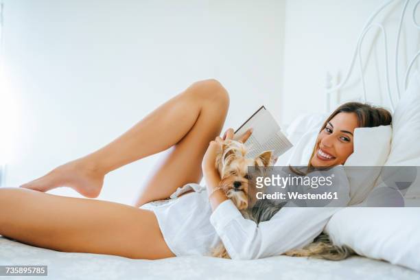 happy woman lying on bed with her yorkshire terrier and a book - yorkshire terrier - fotografias e filmes do acervo
