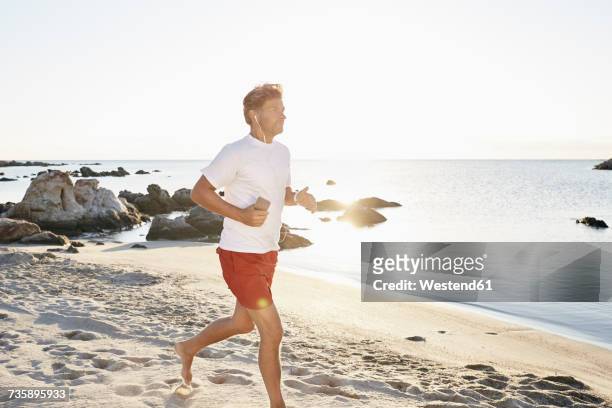 mature man jogging on the beach while listening music with smartphone and earphones - passenger train stockfoto's en -beelden