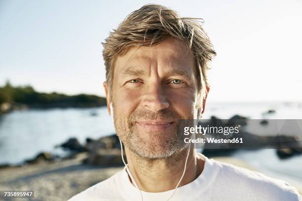 portrait of confident mature man with earphones on the beach - knappe man stockfoto's en -beelden