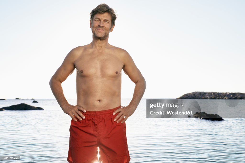 Portrait of confident mature man wearing trunks standing at waterside