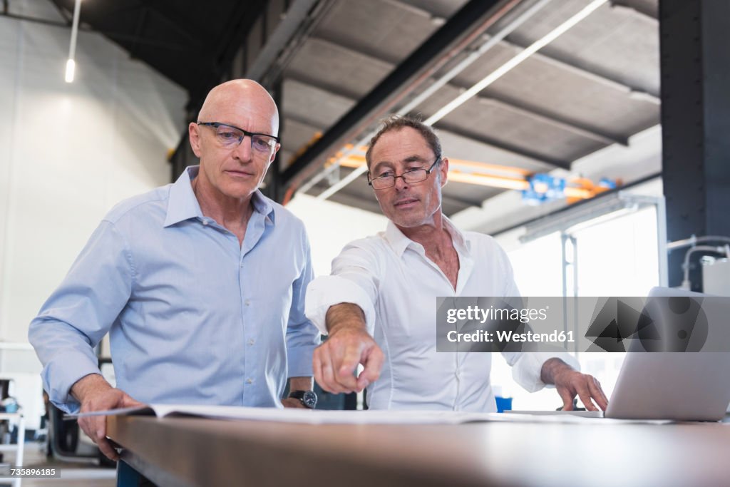 Two businessmen looking at plan on table in factory