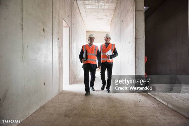 two men wearing safety walking in building under construction - architekt mit plan frontal stock-fotos und bilder