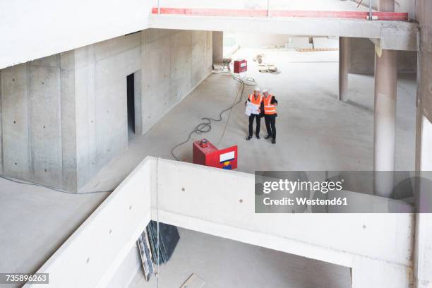 two men with plan wearing safety vests talking in building under construction - baustelle von oben stock-fotos und bilder