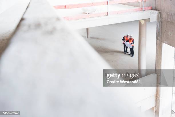 two men with plan wearing safety vests talking in building under construction - distant meeting stock pictures, royalty-free photos & images