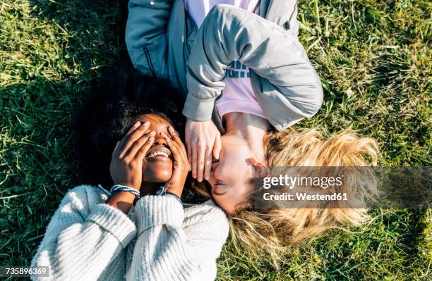 two best friends telling secrets lying in the grass - rumor foto e immagini stock