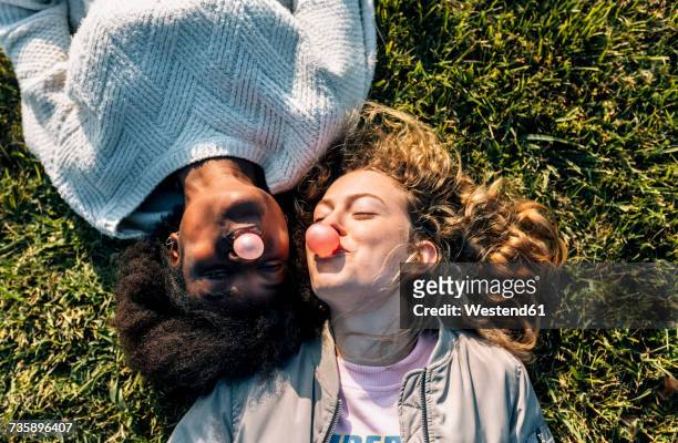 two best friends making a gum bubble lying in the grass - spensieratezza foto e immagini stock