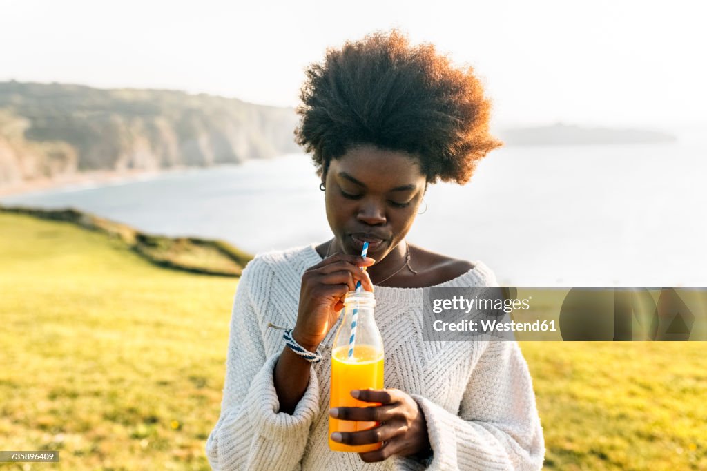 Young woman drinking orange juice at the coast