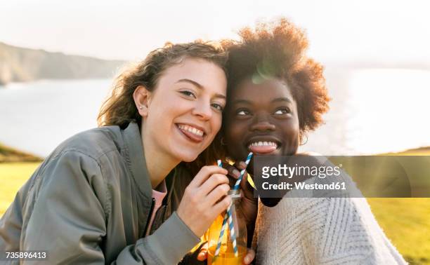 two playful best friends drinking orange juice outdoors - drinking straw stock pictures, royalty-free photos & images