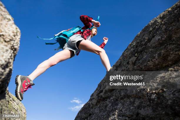 spain, madrid, young woman jumping between rocks during a trekking day - hiking shoes stock-fotos und bilder