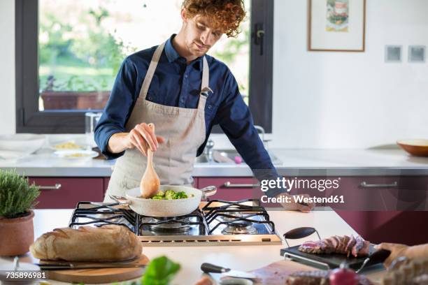 young man preparing broccoli in kitchen - grembiule foto e immagini stock