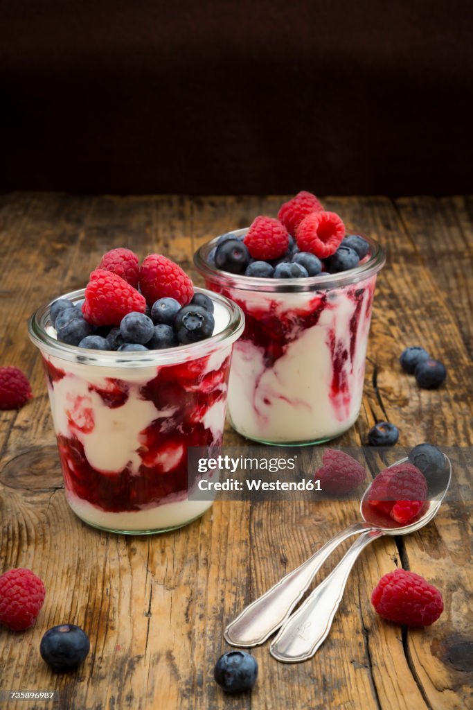 Two glasses of Greek yogurt with berry groats, fresh blueberries and raspberries on wood