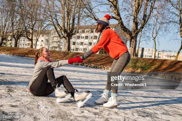 woman helping ice skating friend getting up on canal - doing a favor stockfoto's en -beelden