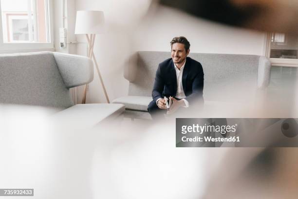 smiling businessman with notebook on couch - differential focus stock pictures, royalty-free photos & images
