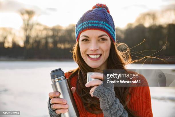 portrait of smiling woman drinking hot beverage from thermos flask outdoors in winter - cologne winter stock pictures, royalty-free photos & images