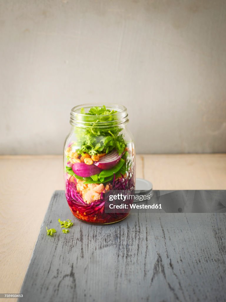Preserving jar of raw food with fried salmon, chili sauce and peanuts
