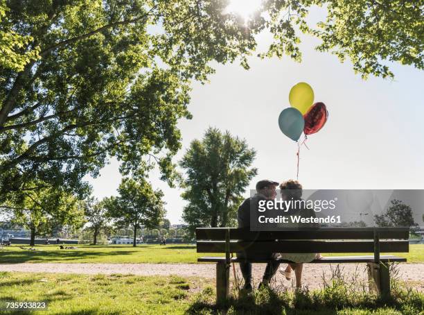 happy senior couple with balloons sitting on bench in a park - bench park stock-fotos und bilder