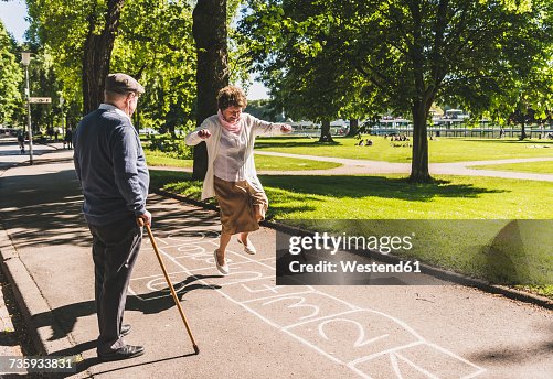 Senior woman playing hopscotch while husband watching her Senior woman playing hopscotch while husband watching her