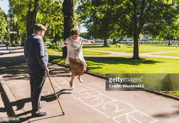 senior woman playing hopscotch while husband watching her - senior adult stock-fotos und bilder
