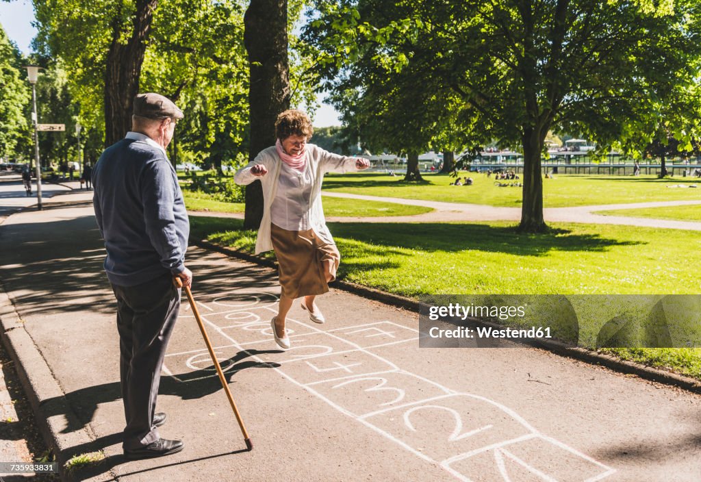 Senior woman playing hopscotch while husband watching her