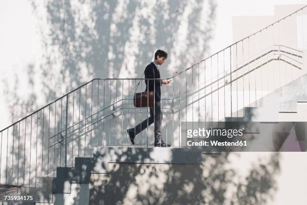 young man in suit walking on stairs and looking at cell phone - businessman in suit ストックフォトと画像