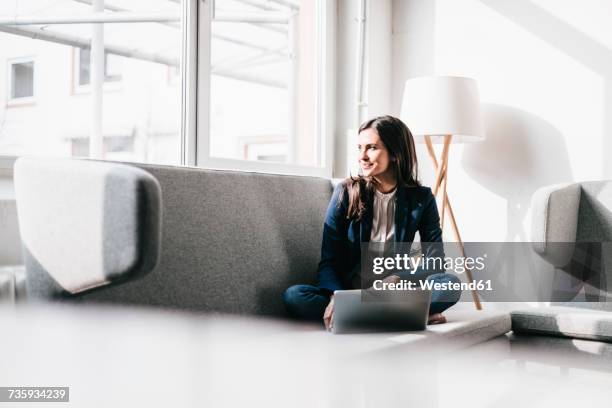 smiling businesswoman using laptop on couch - couch notebook stock-fotos und bilder