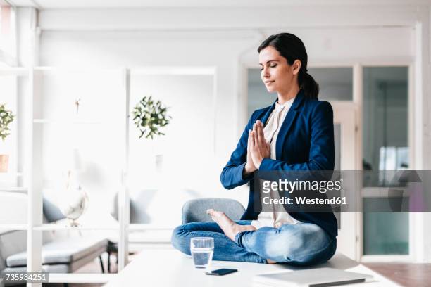 businesswoman sitting on table meditating - office yoga stock pictures, royalty-free photos & images