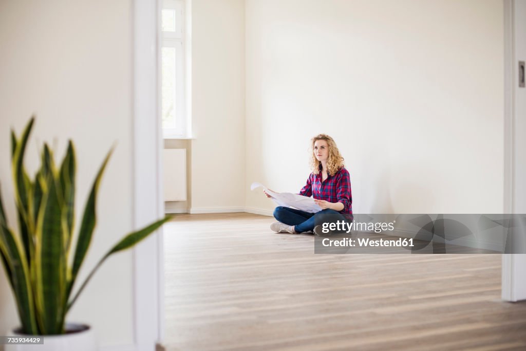 Young woman in new home sitting on floor with plan