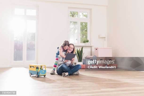 happy girl and mother with tablet in empty apartment - small child sitting on floor stockfoto's en -beelden