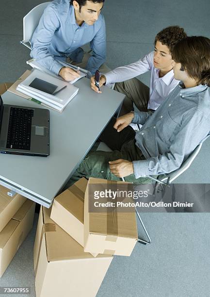 three male colleagues grouped around desk, surrounded by cardboard boxes - makeshift desk stock pictures, royalty-free photos & images