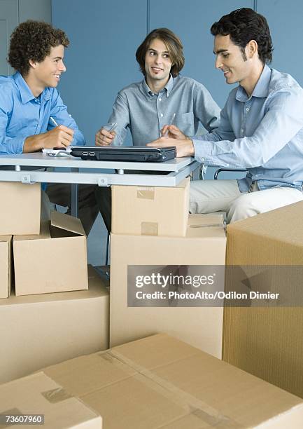 three male colleagues working at table, cardboard boxes in foreground - makeshift office stock pictures, royalty-free photos & images