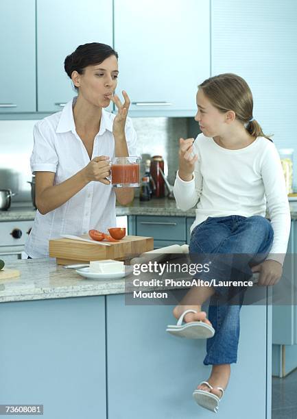 girl sitting on kitchen counter while mother holds up container of tomato sauce - licking finger stock pictures, royalty-free photos & images