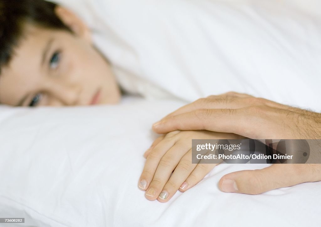 Child lying in bed, father's hand on child's