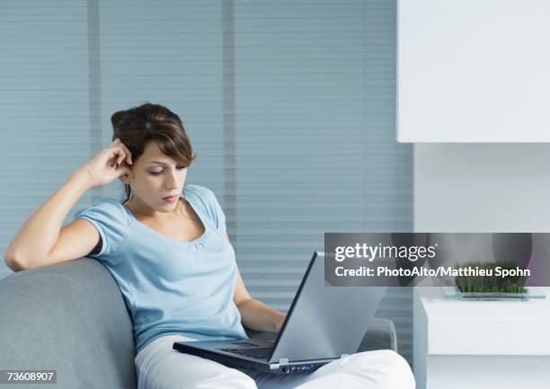 young woman sitting on sofa, using laptop - short sleeved stock pictures, royalty-free photos & images
