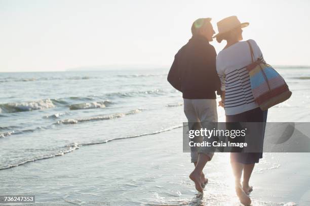 barefoot mature couple walking on sunset beach - camber sands stockfoto's en -beelden