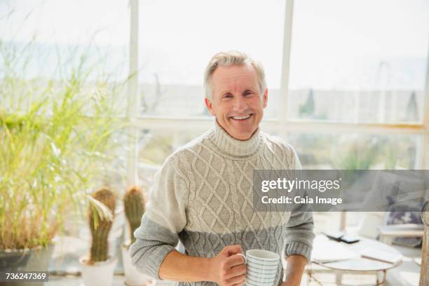 portrait smiling senior man drinking coffee in beach house sunny sun porch - cuello alto fotografías e imágenes de stock