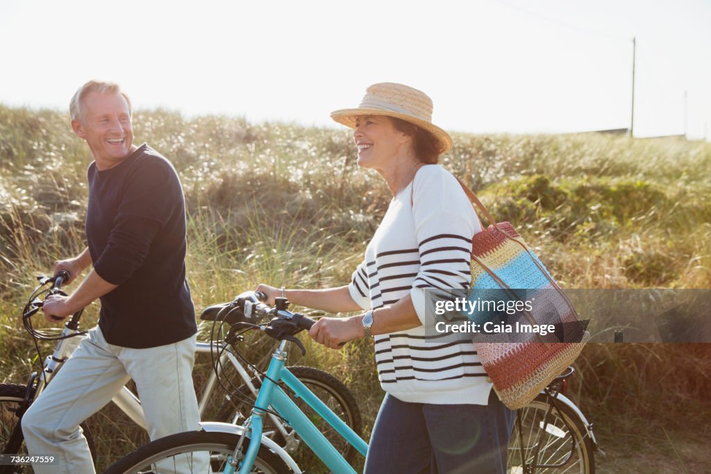 Mature couple walking bicycles on sunny beach grass path
