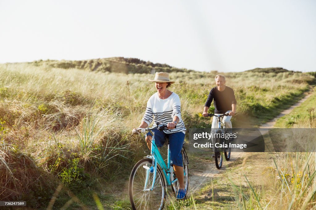 Mature couple riding bicycles on sunny beach grass path