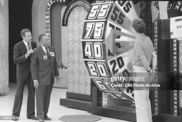 American game show host Bob Barker advises a contestant about spinning the big wheel as another contestant looks on during the 15th Anniversary...